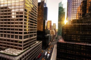 A high-rise office building in New York City with large reflective glass windows, capturing the bright sun and the surrounding skyline.