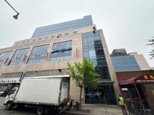 Wide street view of NYC office tower with rope-access window cleaners working high up.