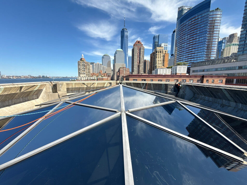 Total Window Service rope access crew installing Solar Gard Sentinel Plus exterior film on the Museum of Jewish Heritage skylight dome — Lower Manhattan skyline with One World Trade Center in background